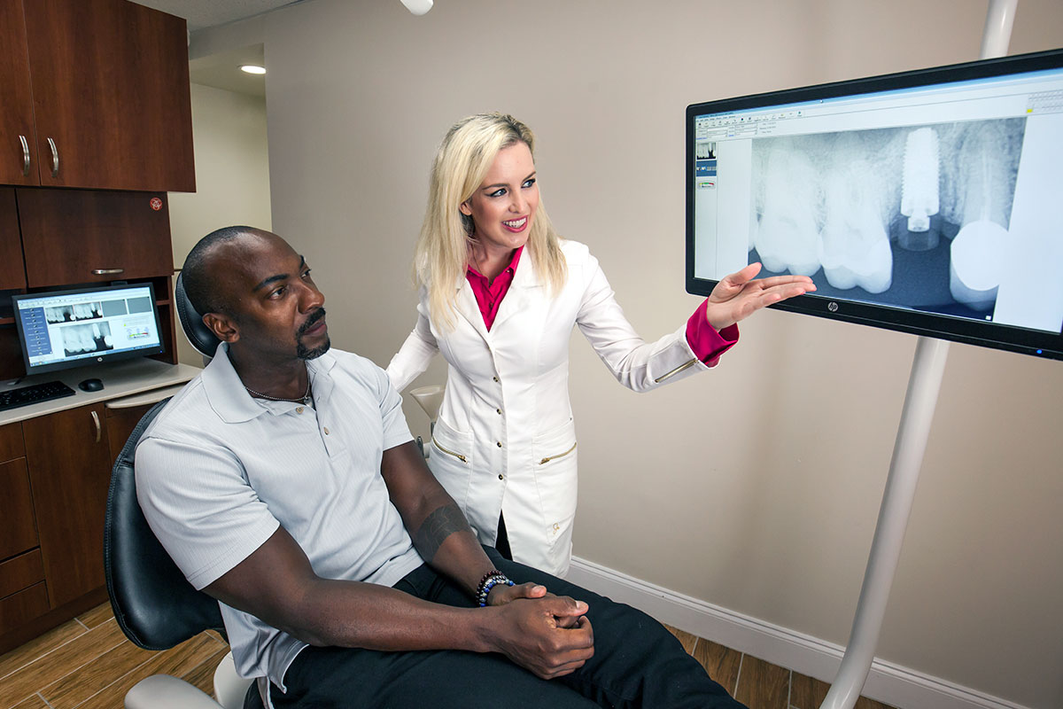 Dentist shows patient a dental implant on monitor during a consultation.