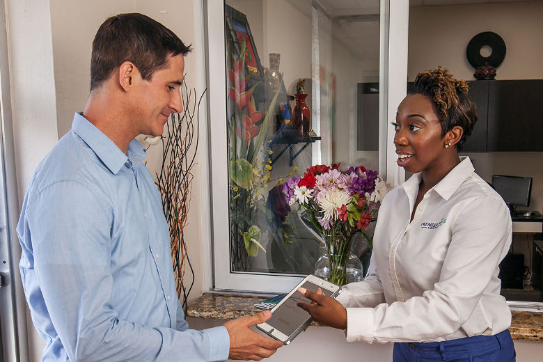 A receptionist hands a patient a tablet to fill out patient information.